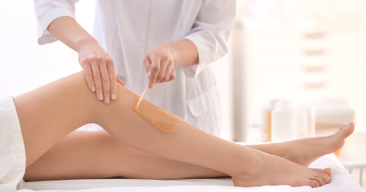 A cosmetologist applying warm waxing to a woman's lower leg with a wooden spatula during a hair removal treatment in a spa or salon in Waukee, IA